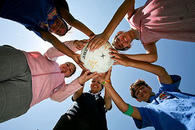 A group of First Nations people standing in a circle, holding a netball and smiling at the camera.
