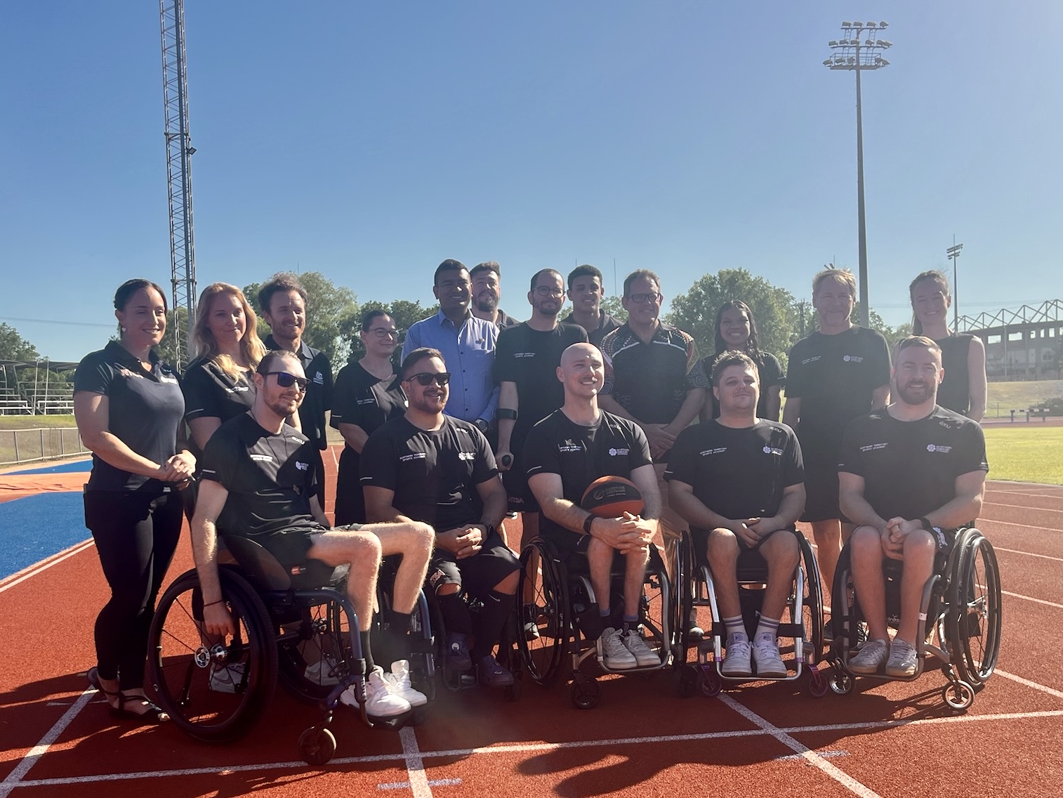 People standing and in wheelchairs on running track