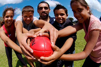 Australian Rules Football player Adam Goodes Sydney Swans with children holding an AFL ball