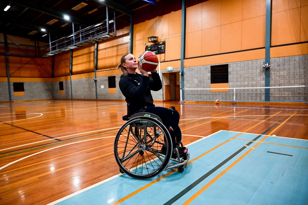 Female para athlete Georgina Gott in a wheelchair preparing to shoot a basketball into the hoop on a basketball court.