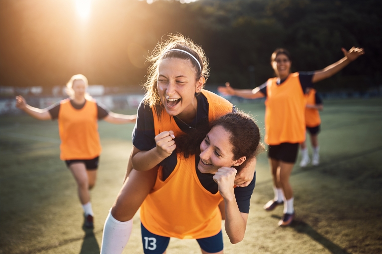 A group of female soccer players in orange team singlets celebrate.