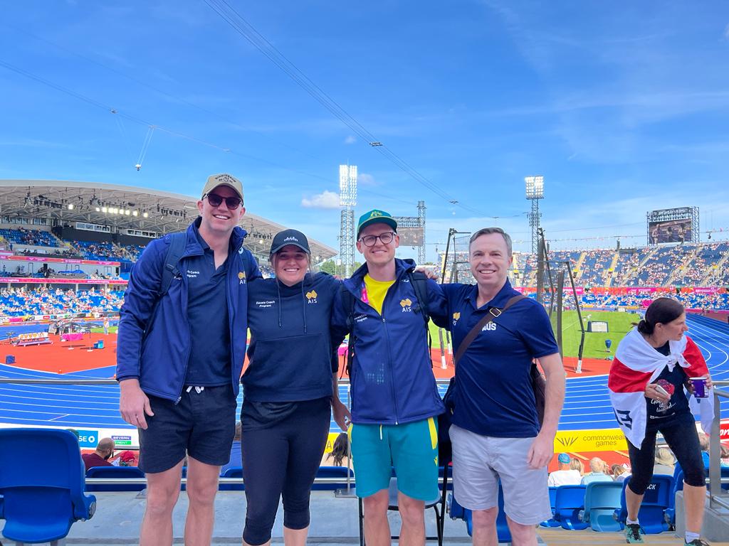 Coaches stand in front of an athletics stadium.