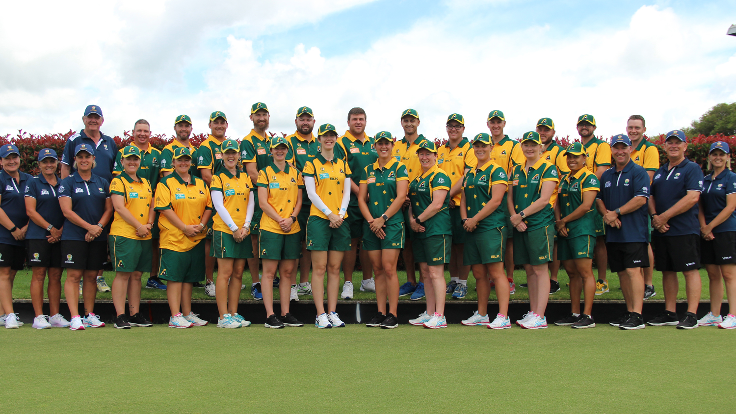 Bowls athletes stand on green grass in two rows
