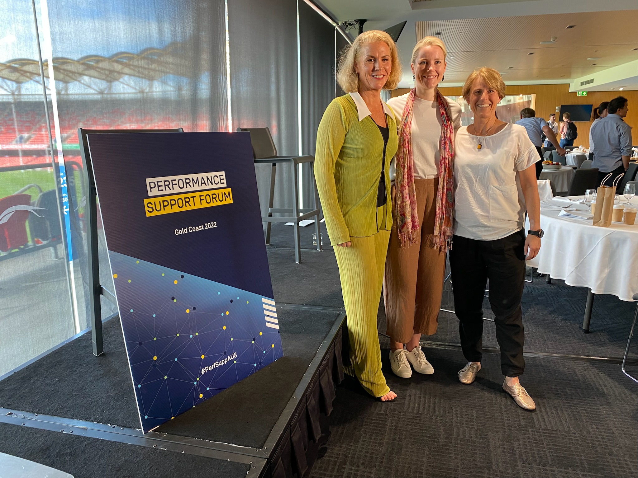 Three females pose in front of the Performance Support Forum sign