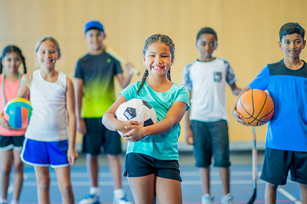 A group of children holding an assortment of sports equipment and balls