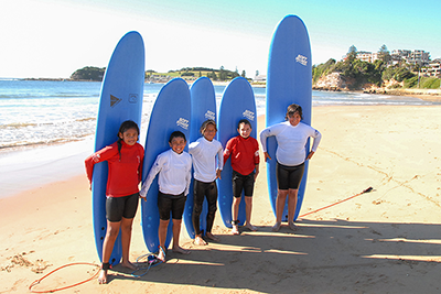 First Nations kids standing in front of surfboards