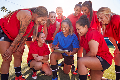 Coach With Digital Tablet Discussing Tactics With Womens Football Team at Training