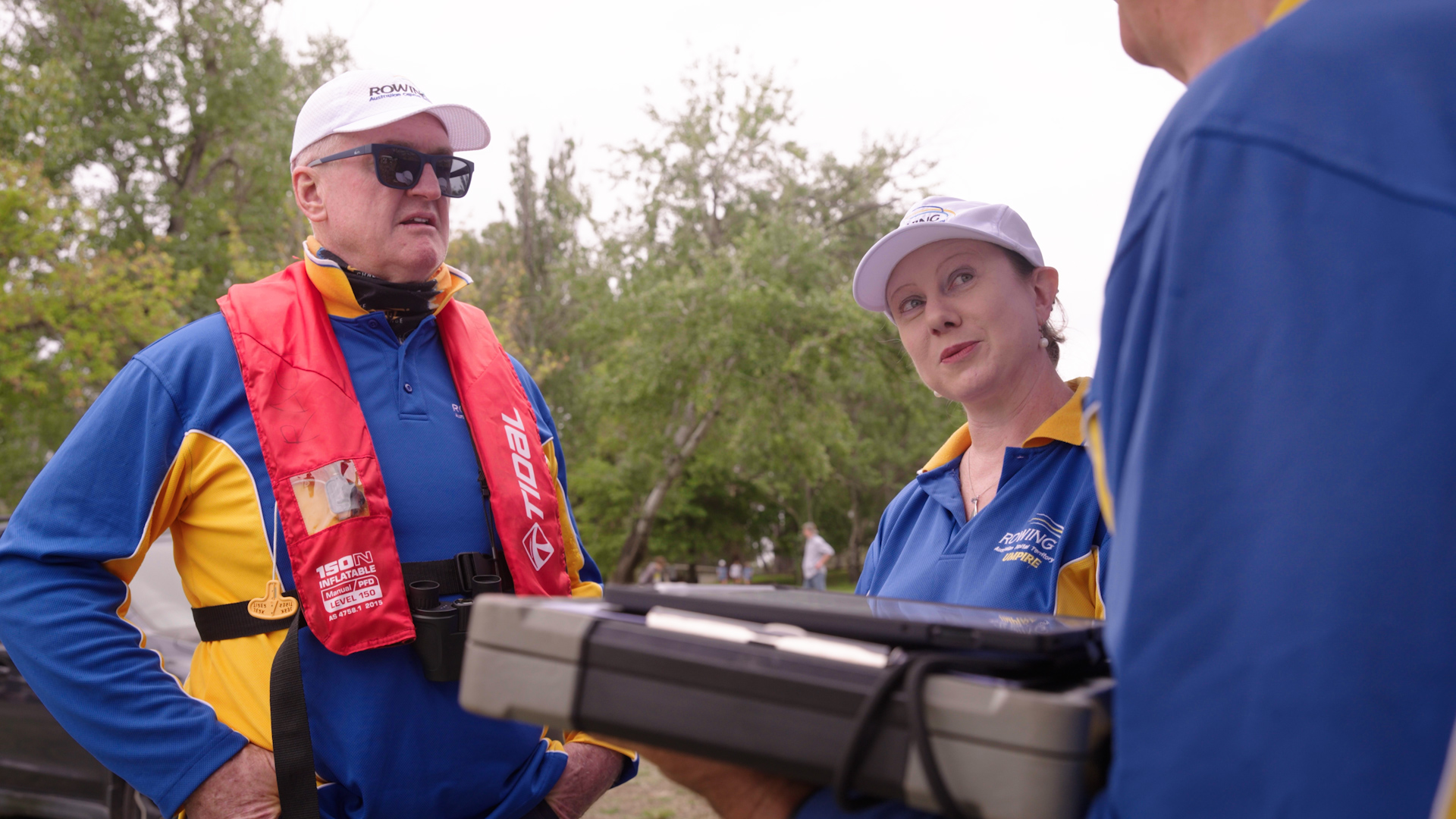 A rowing official mentor in the middle listens to an official on the right and another official listens on the left