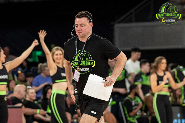 A Heartland Crew member runs across the court with cheerleaders in the background.