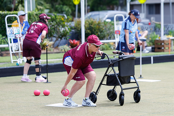 A competitor holding onto an assistive walker frame while bowling her bowl