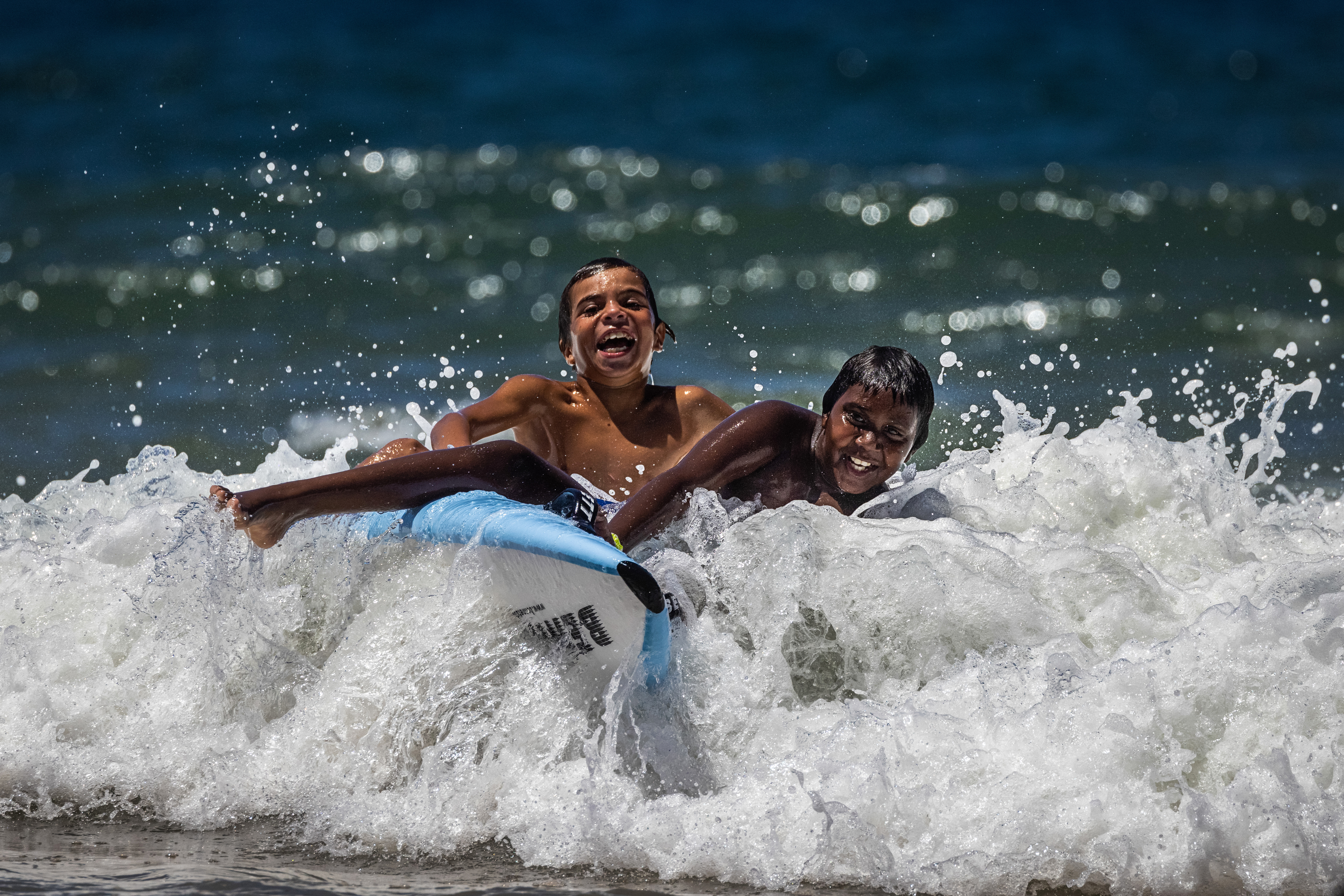 Two boys laughing while riding a wave to the shore.