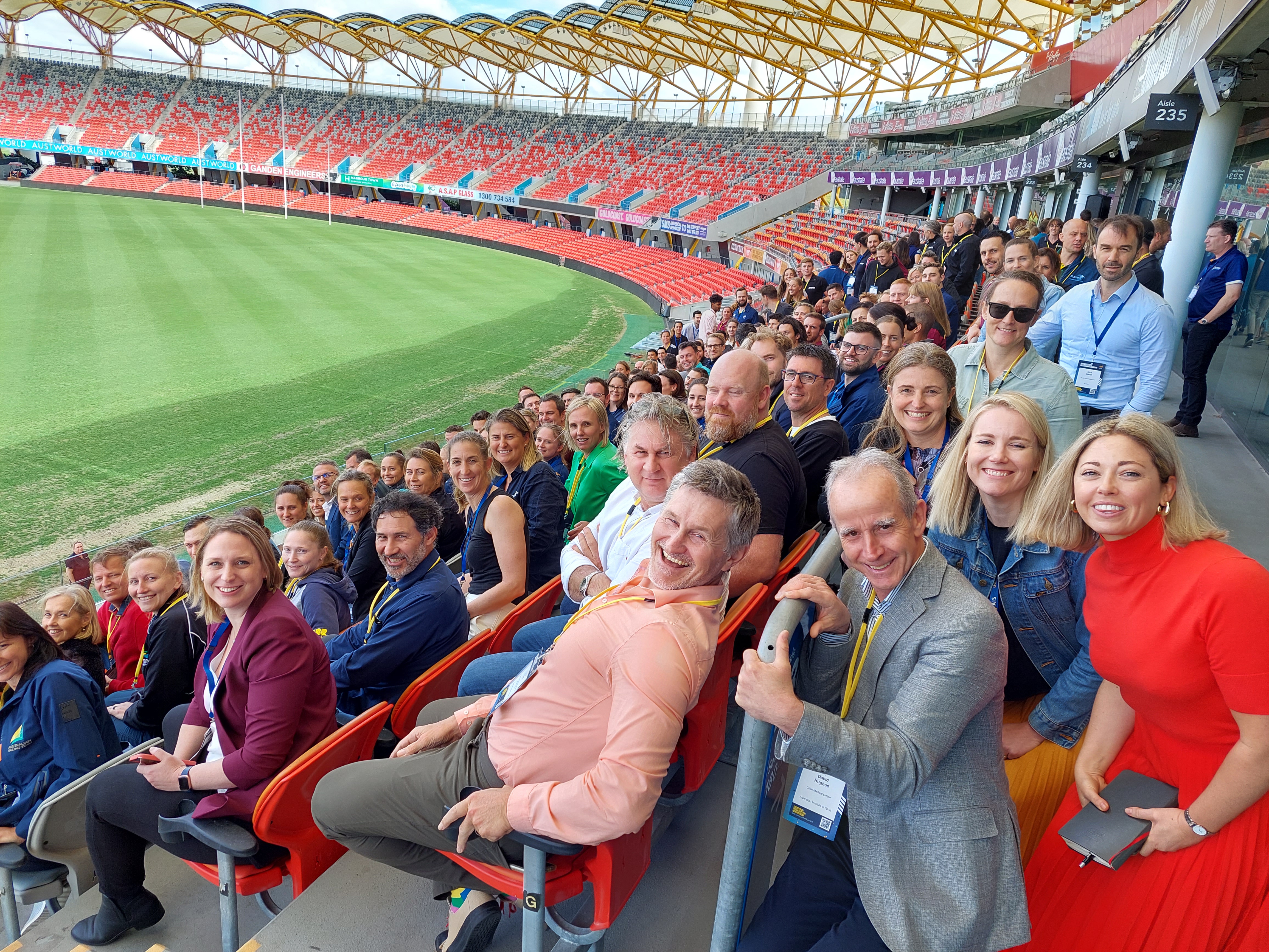 All the participants sitting in the stadium with the oval in the background