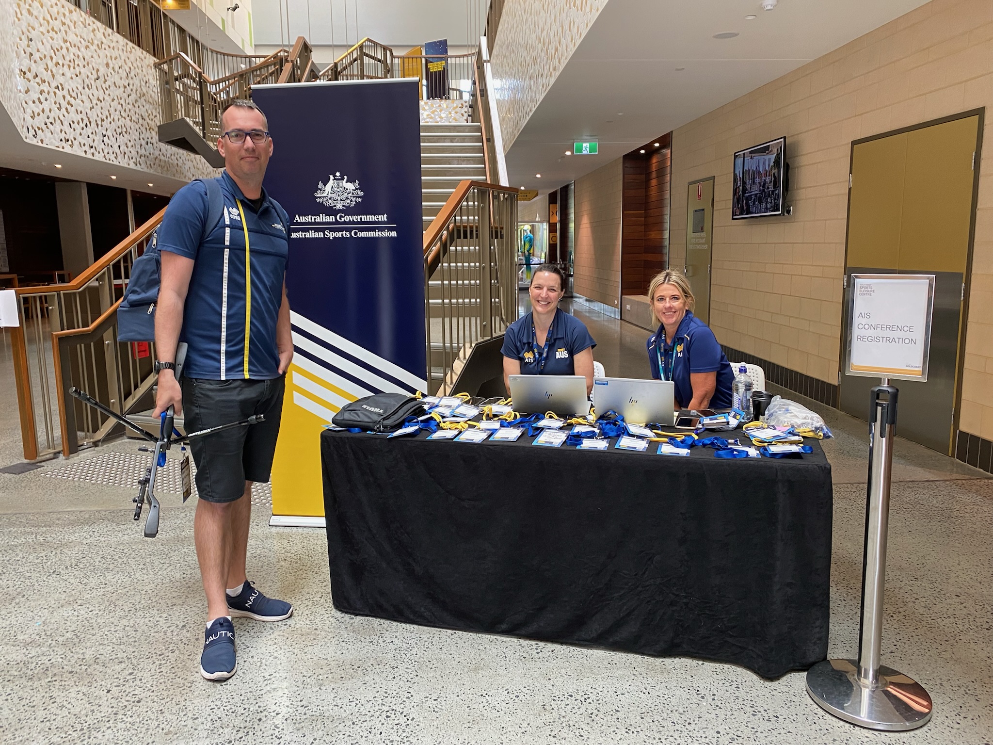 Two females seated at the entrance of the conference welcoming a gentleman