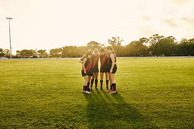A group of community AFL players standing in a huddle on a grass field before play