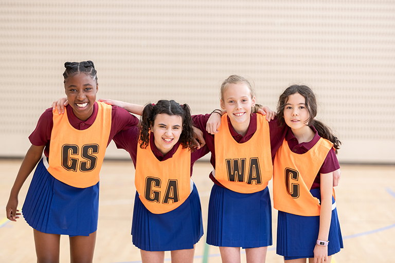 Four girls wearing netball bibs smiling at the camera.