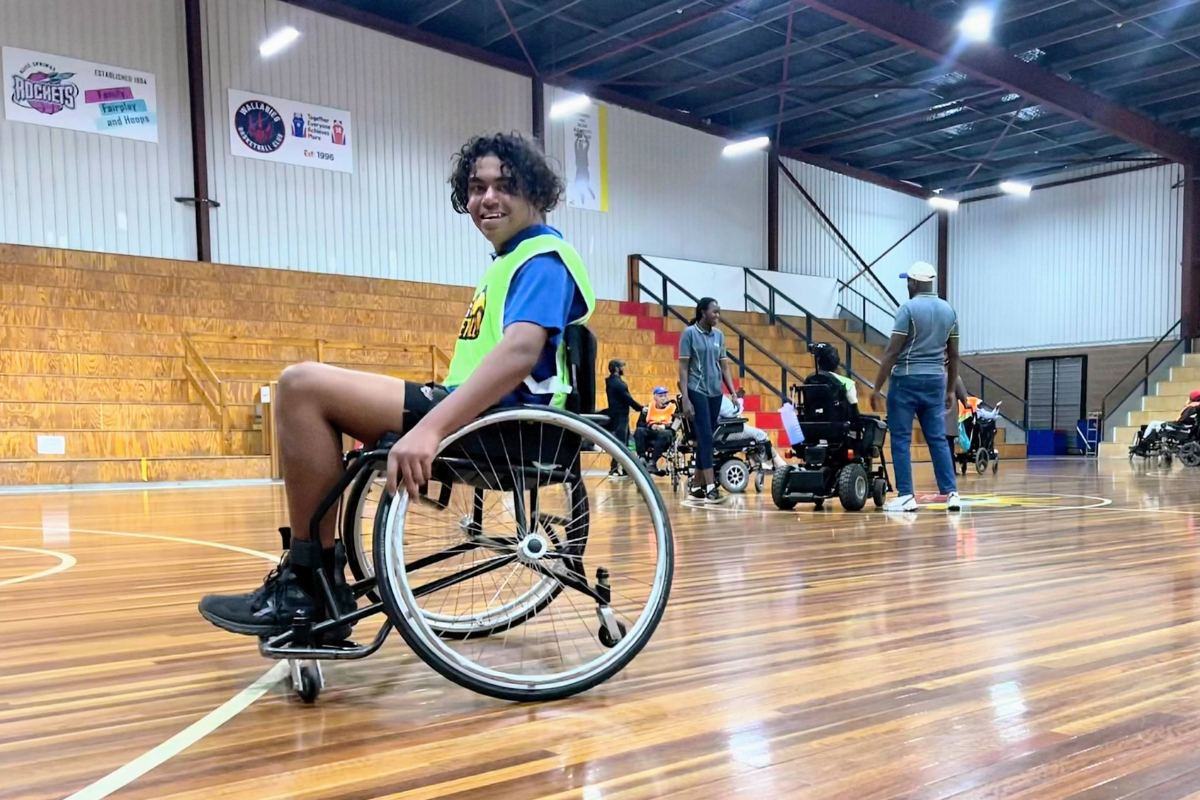 Teenage boy using a wheelchair on an indoor basketball court.