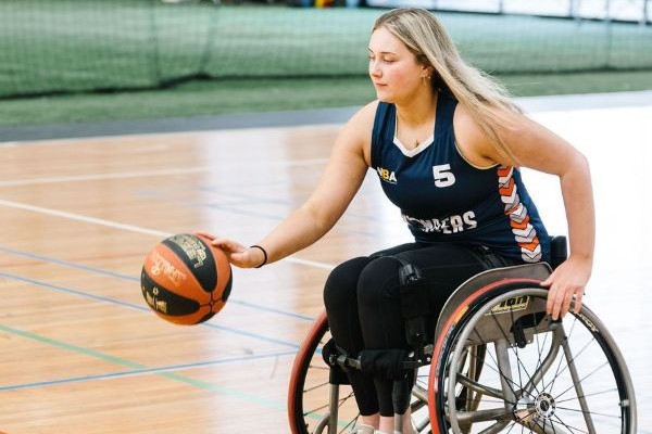 Young lady dribbling a basketball on a court, using a wheelchair