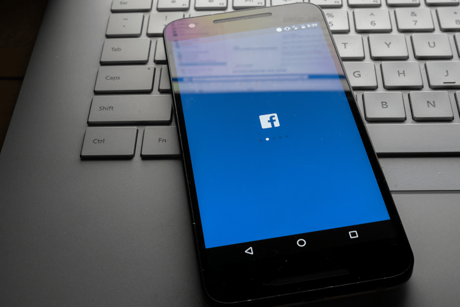 mobile phone displaying Facebook logo rests on laptop keyboard.
