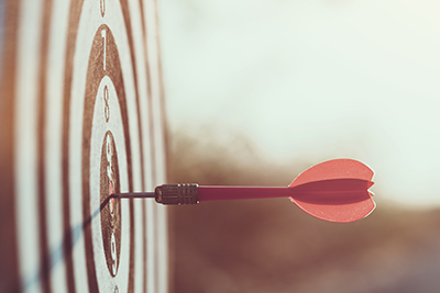 A red dart embedded in the bullseye of an archery target