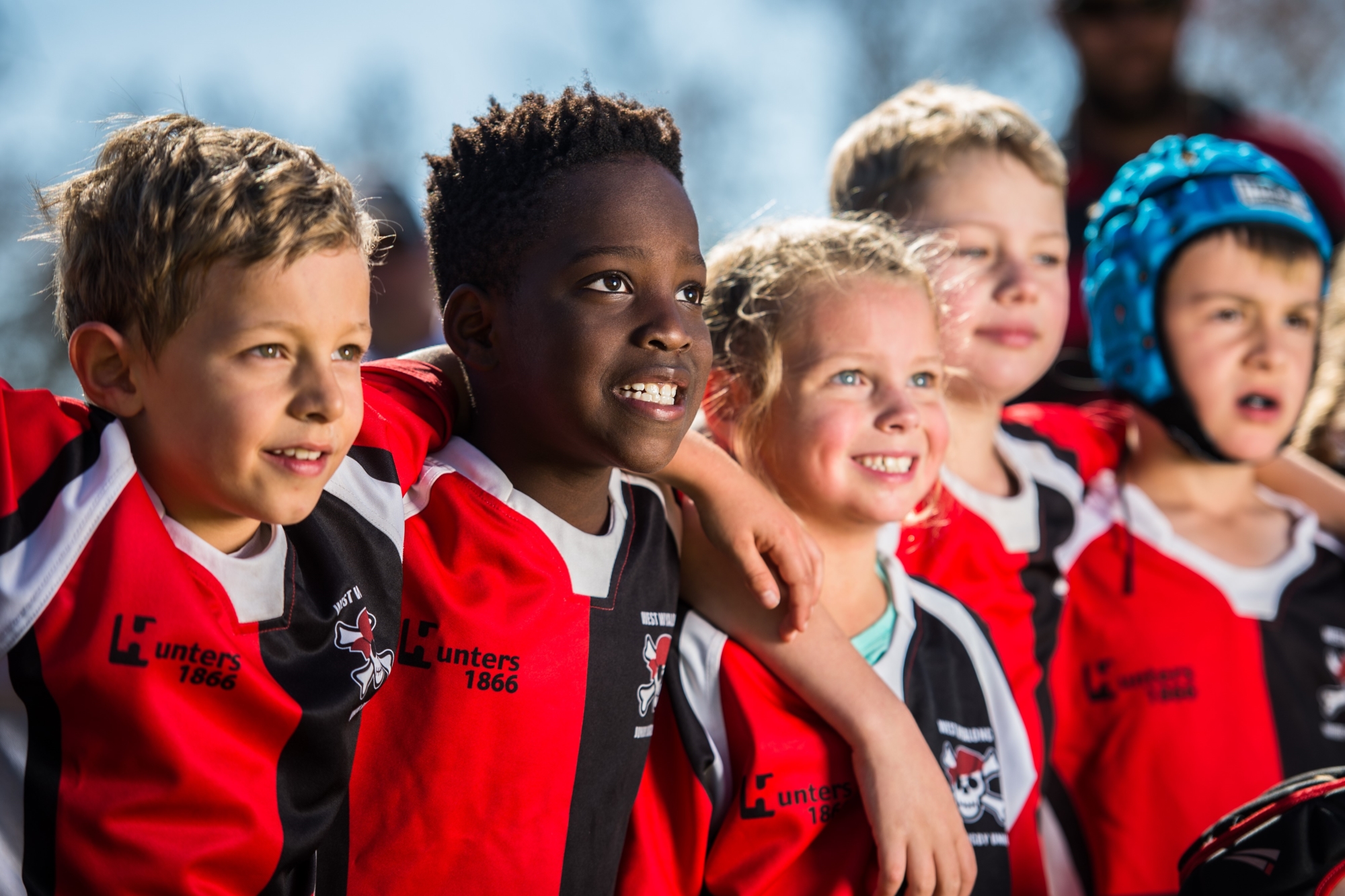 Children in Rugby uniforms stand arm in arm.