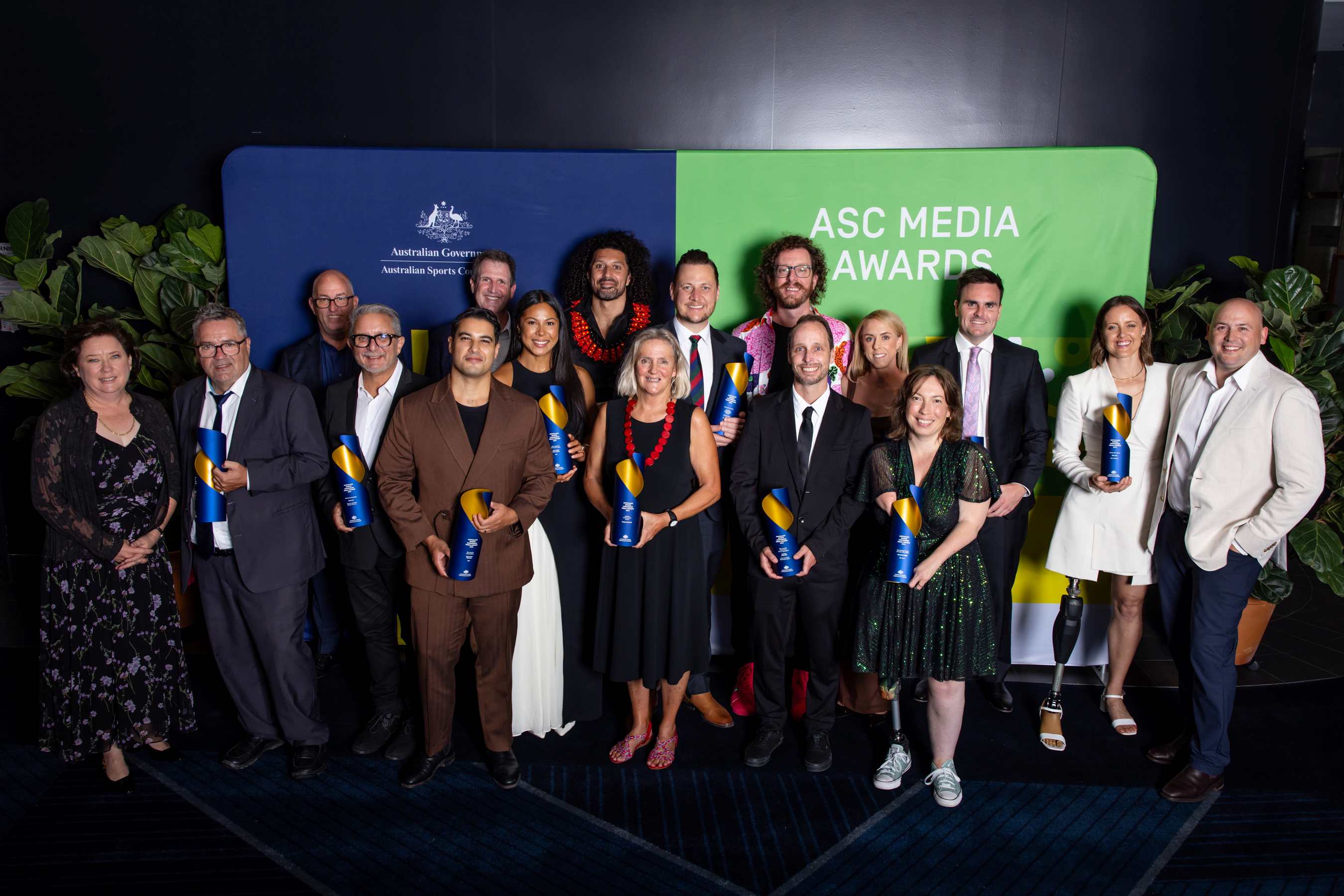 The 17 winners of the 2024 Australian Sports Commission Media Awards standing in front of a media wall in Sydney, 2025