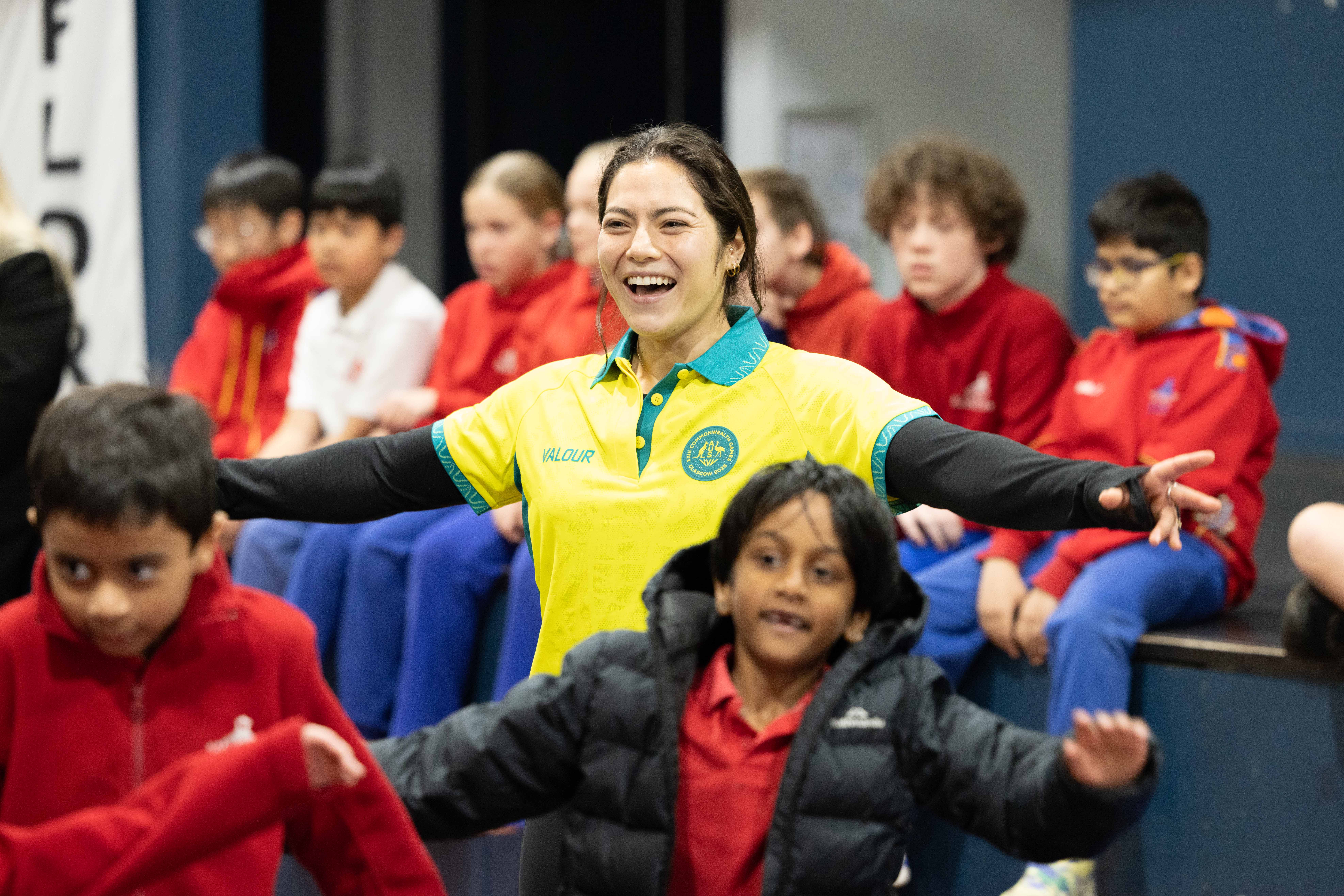 Australian Commonwealth Games gymnast Georgia Godwin standing with her arms out surrounded by year 1 and 2 students at a Sporting Schools gymnastics session