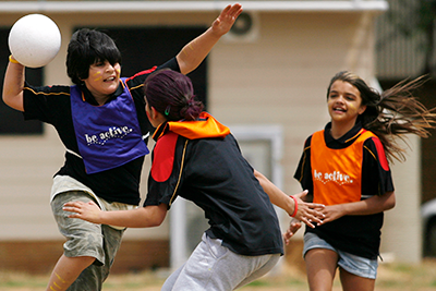 Children playing a ball game outdoors, wearing team bibs and actively moving during play.