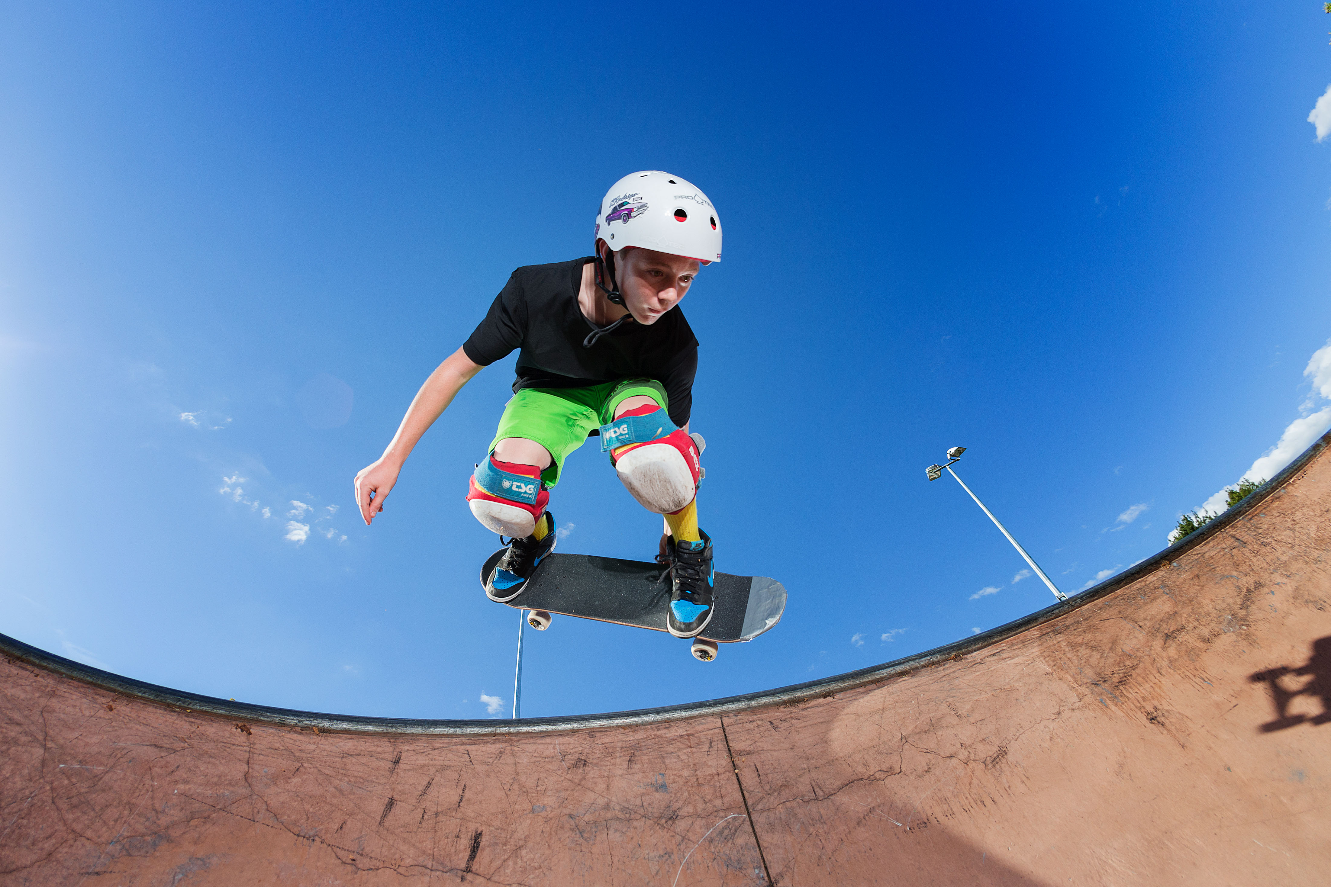 Photo of a boy wearing a helmet and knee pads doing a skateboarding trick in a skateboarding park