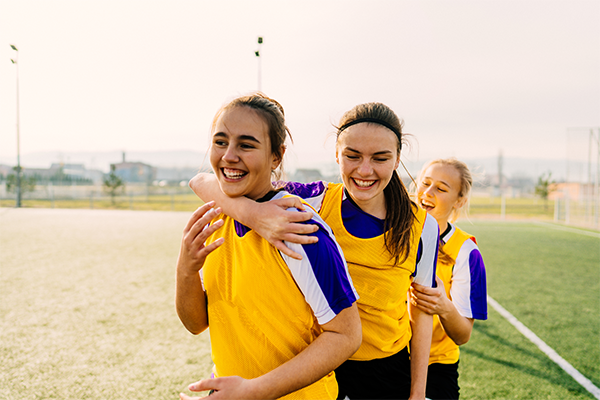 Three young people in yellow and purple sports uniforms walk together on an outdoor playing field