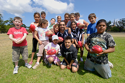Group of kids huddled around Adam Goodes