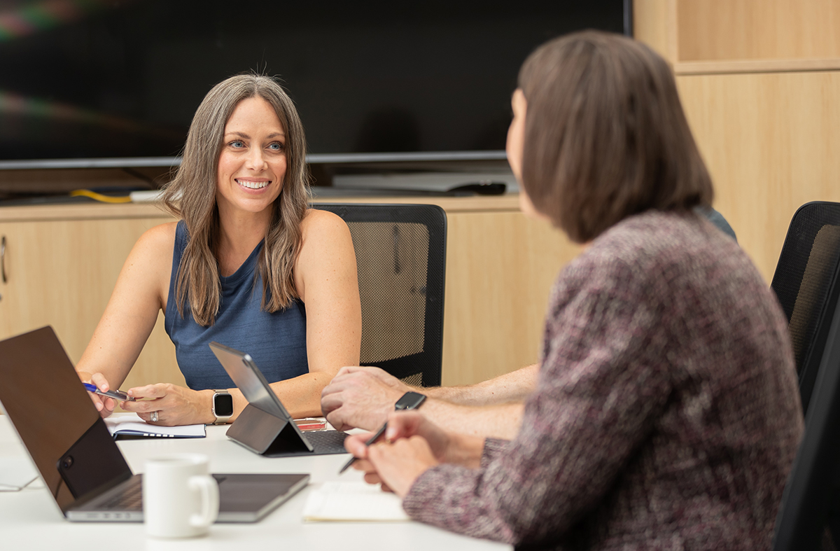 Two women in an office setting sitting in front of a laptop working.