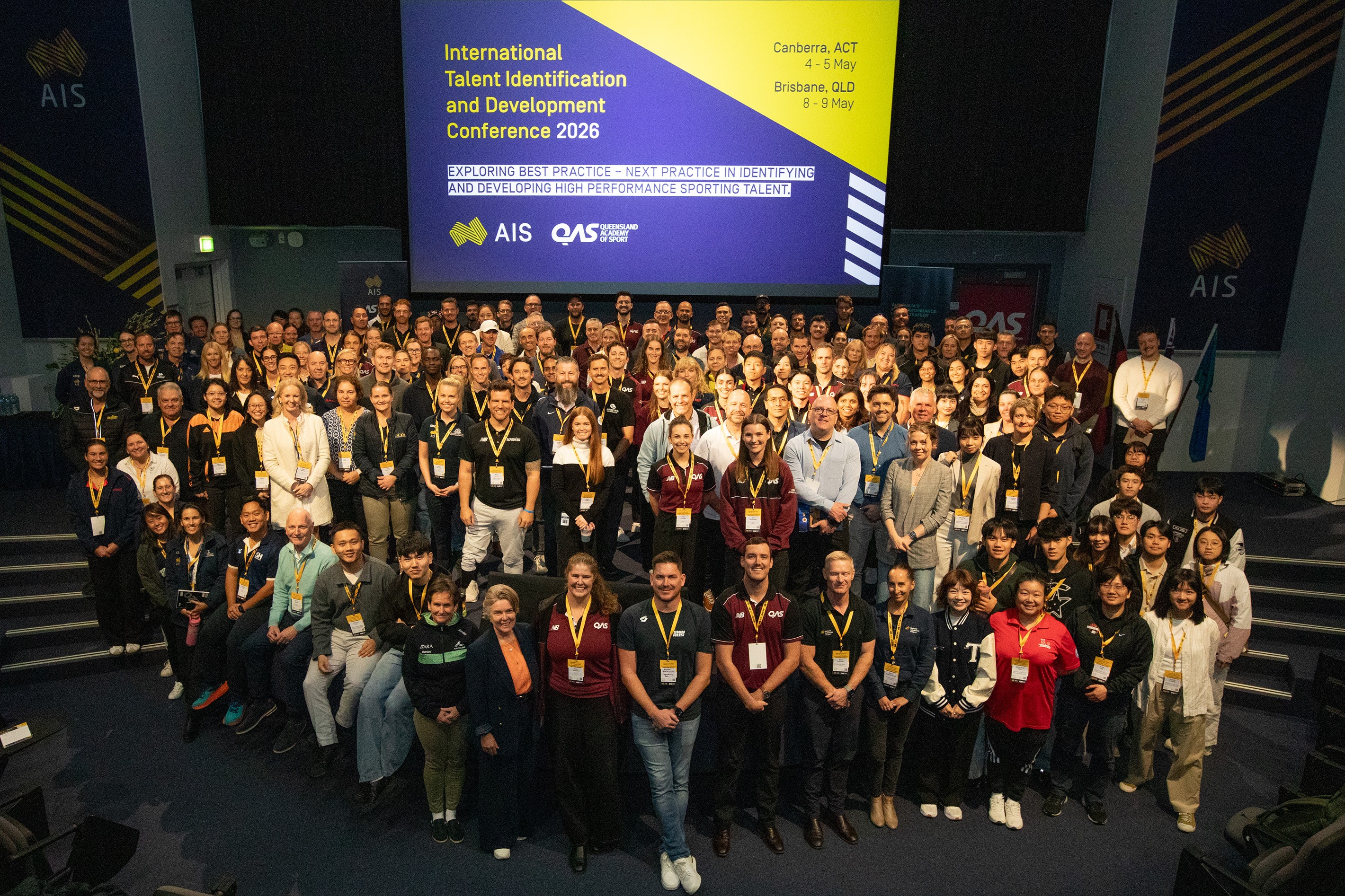 300 delegates at the Talent ID Conference stand on stage at the AIS in front of Conference branding