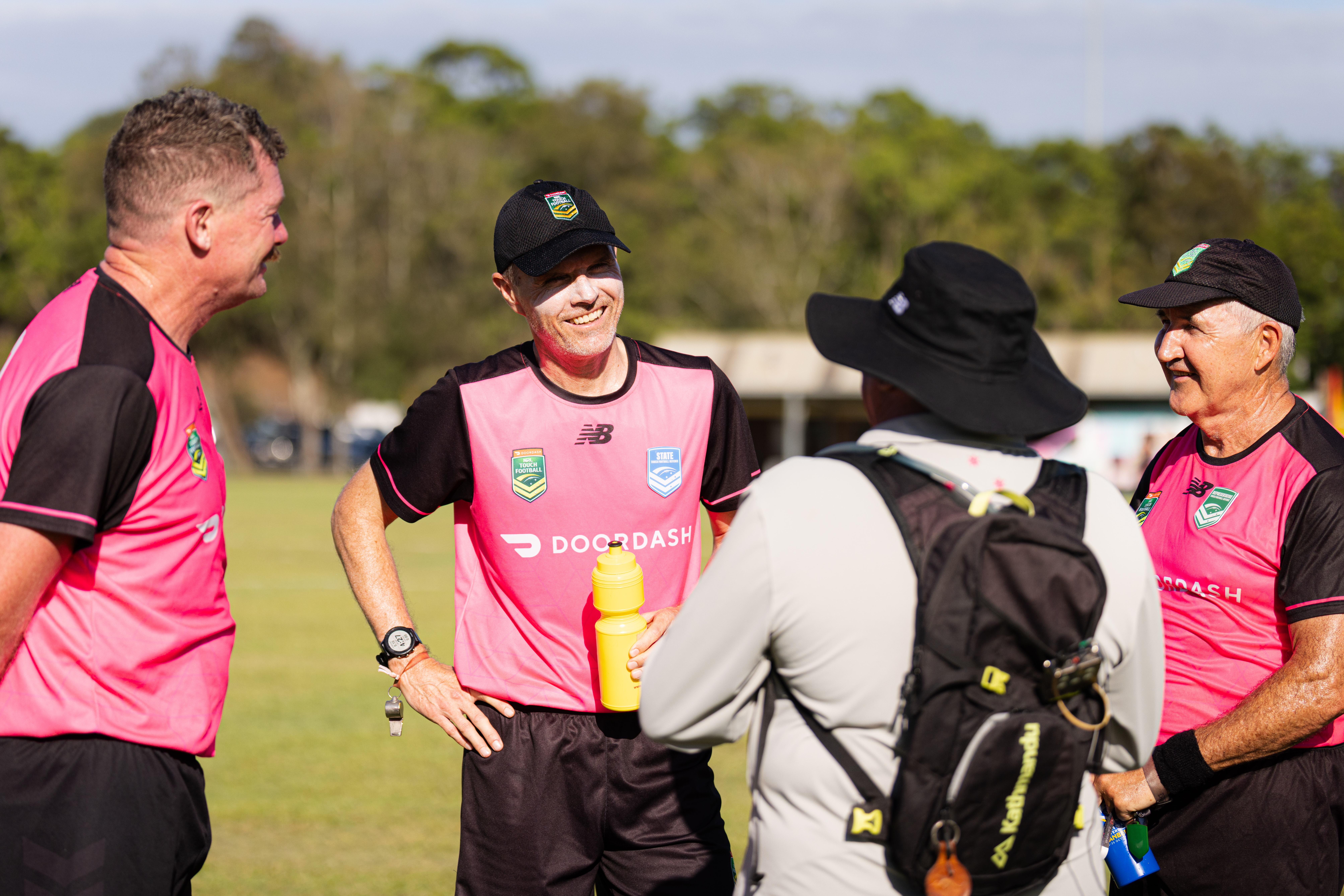 A touch football referee coach with his back to the camera talks with 3 referees
