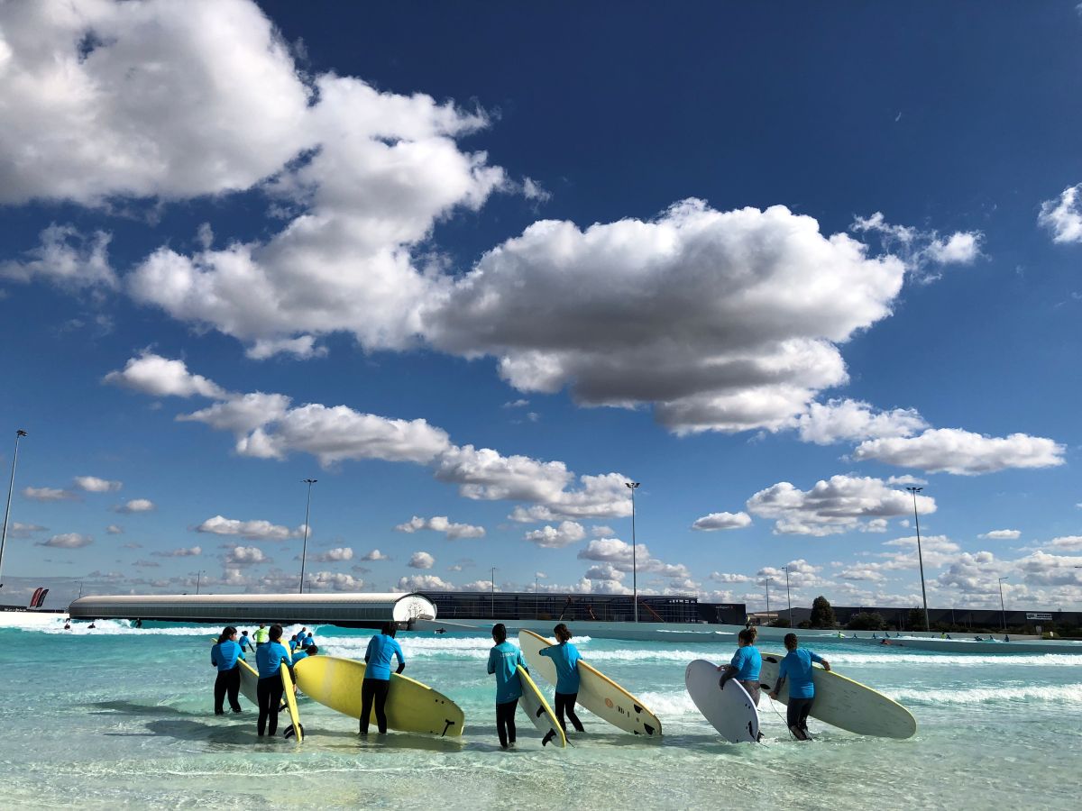 A group of students holding surfboards and looking out to a wave pool as they look for rips and swells so they know where it's safe to surf and play