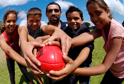 C4S-evidence-first nations-kids holding an Australian Rules football with Adam Goodes