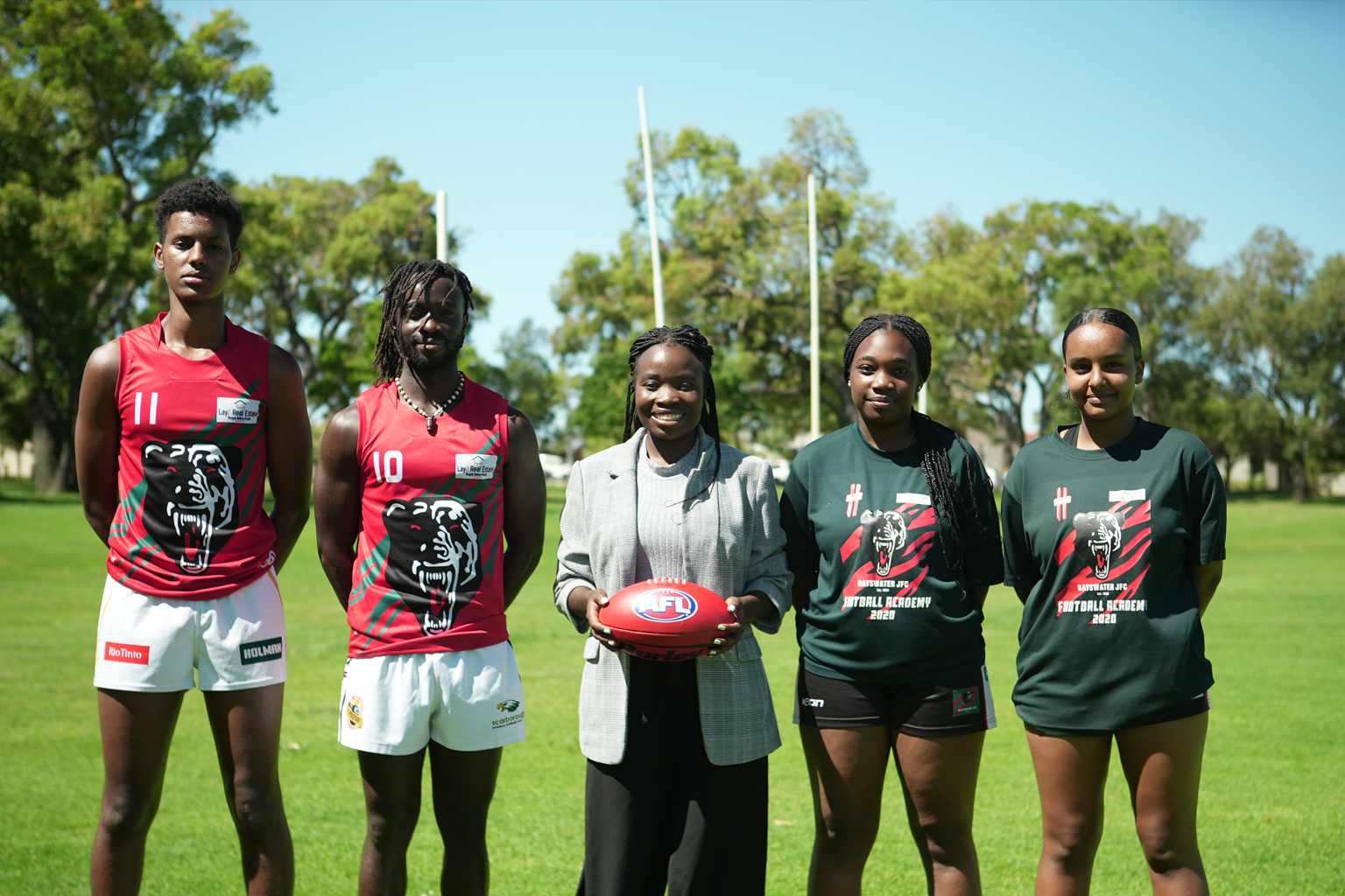 Four Australian football players, two men and two women, stand side-by-side with their coach in the middle.