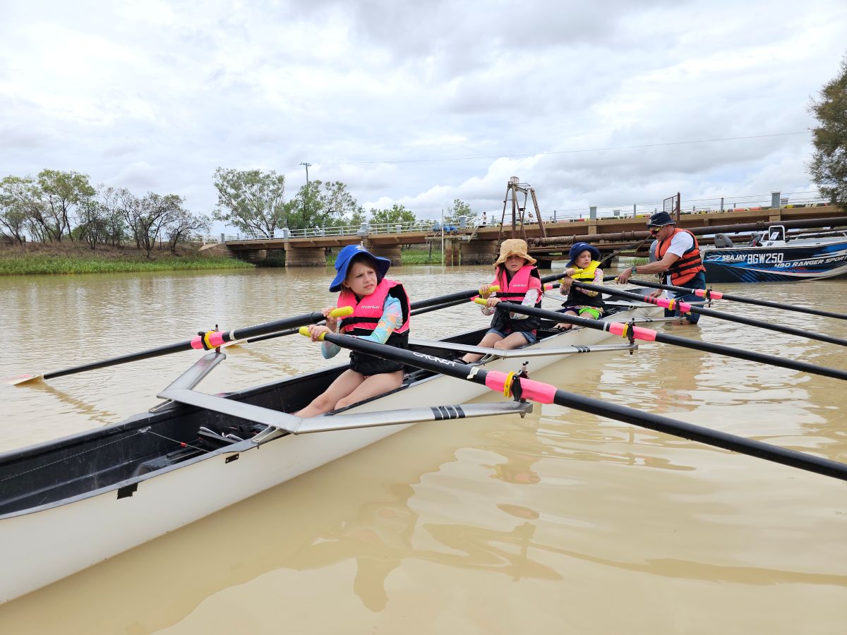 Students using a rowing a performance row boat on a river with the help of coaches