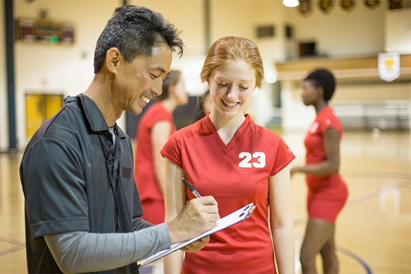 Coach holding a clipboard and taking notes while speaking with a volleyball player