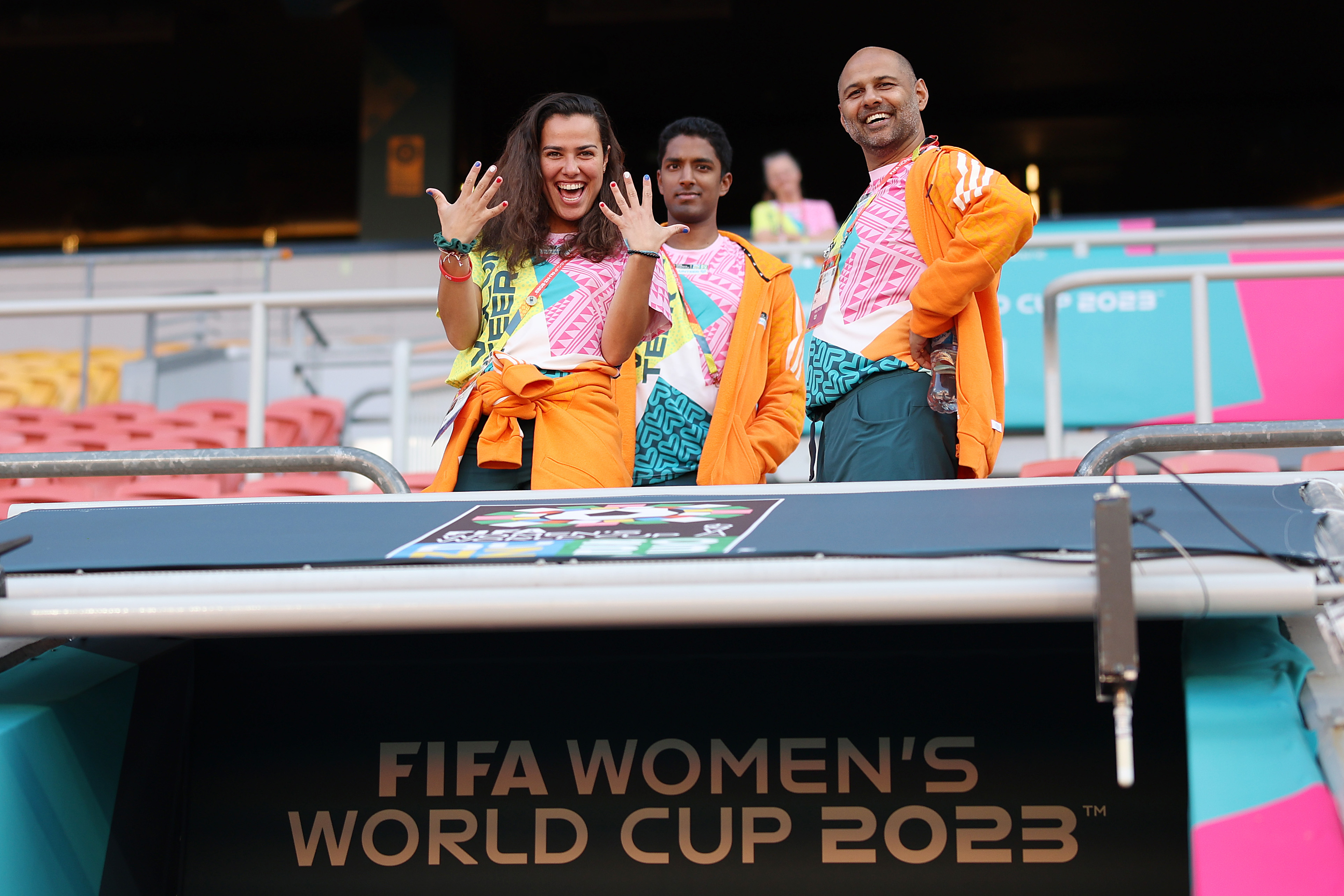 Three volunteers standing in a stadium with a 'FIFA Women's World Cup 2023 sign below them