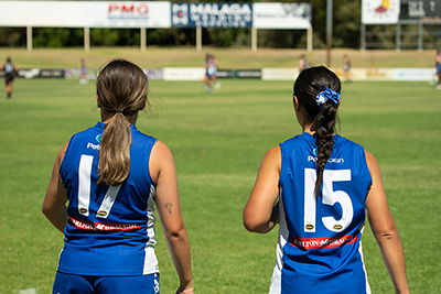 Female AFL players watching a match from the sideline