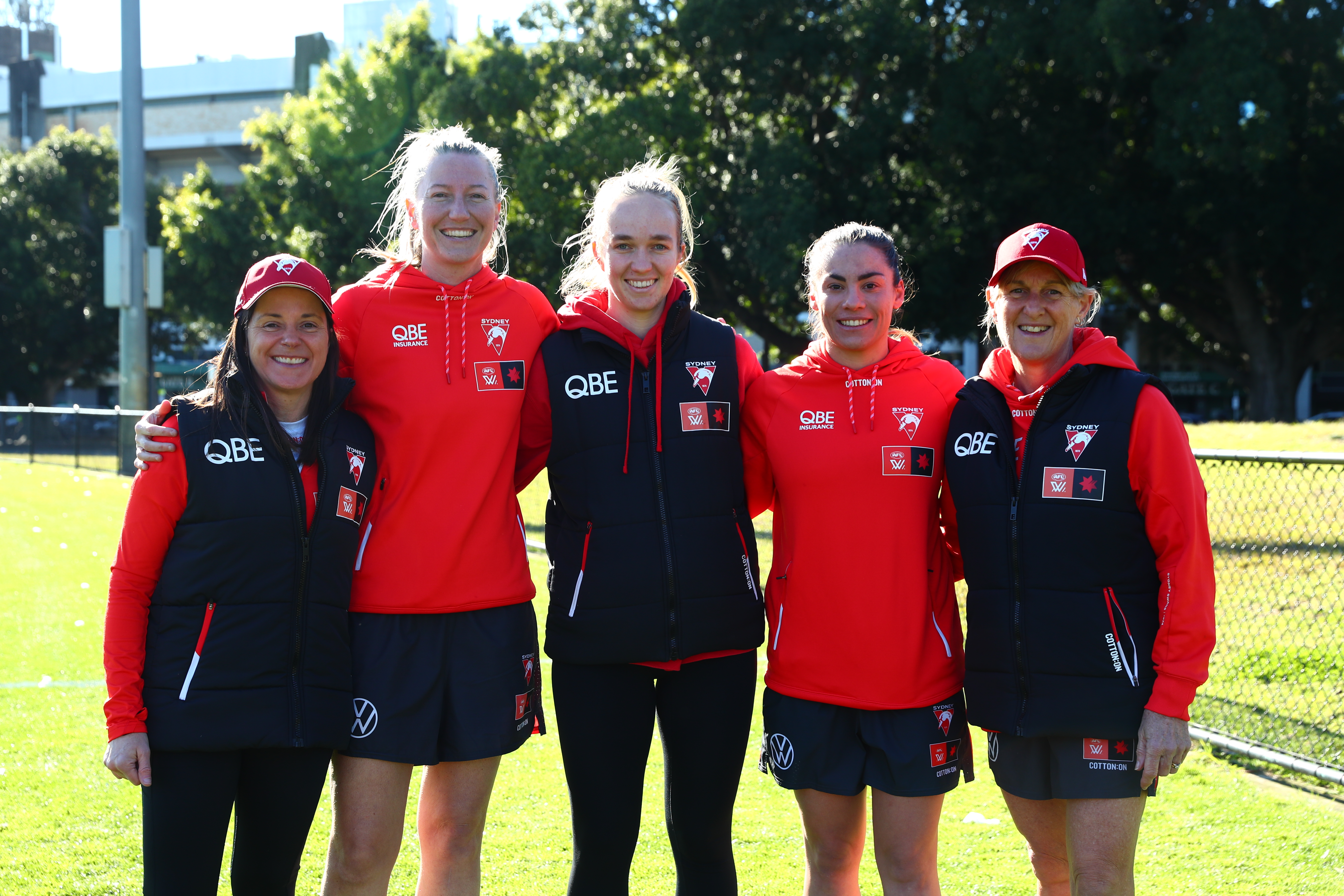 Five members of the Sydney Swans AFLW coaching team standing with their arms around each other.