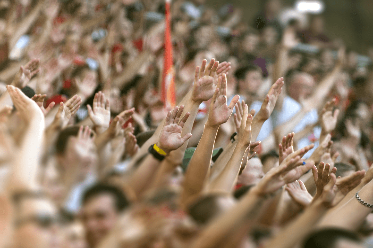 A crowd of spectators in a grandstand all raise their hands.