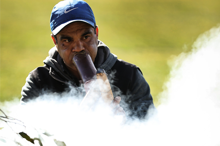 Man playing didgeridoo behind smoke