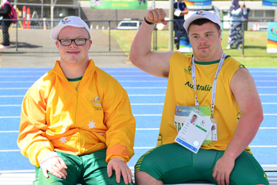 Two athletes with Down syndrome sitting on a bench waiting for their turn to participate at an athletics event.