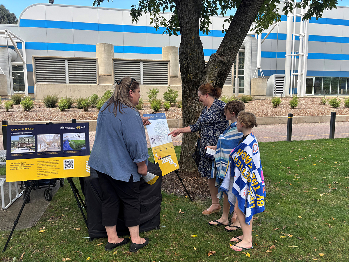 A woman and two children speak to staff at a Podium Project information session held at the AIS Campus.