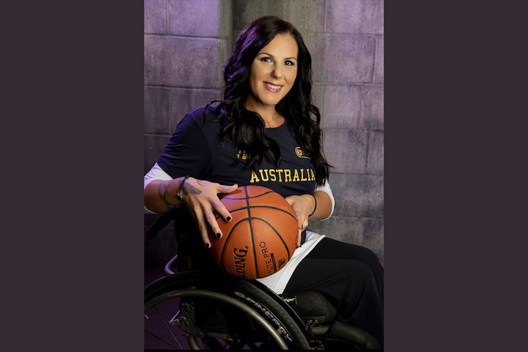 Natalie Curtis holding a basketball, wearing an Australia team T-shirt, in her wheelchair.
