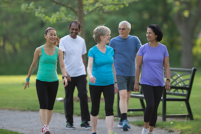 A group of senior adults are walking together on a trail through the park.