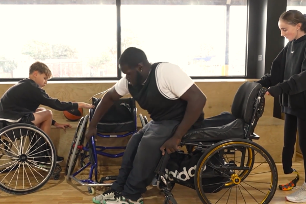 Man getting transferring from a regular to a sport wheelchair with help from 2 other people