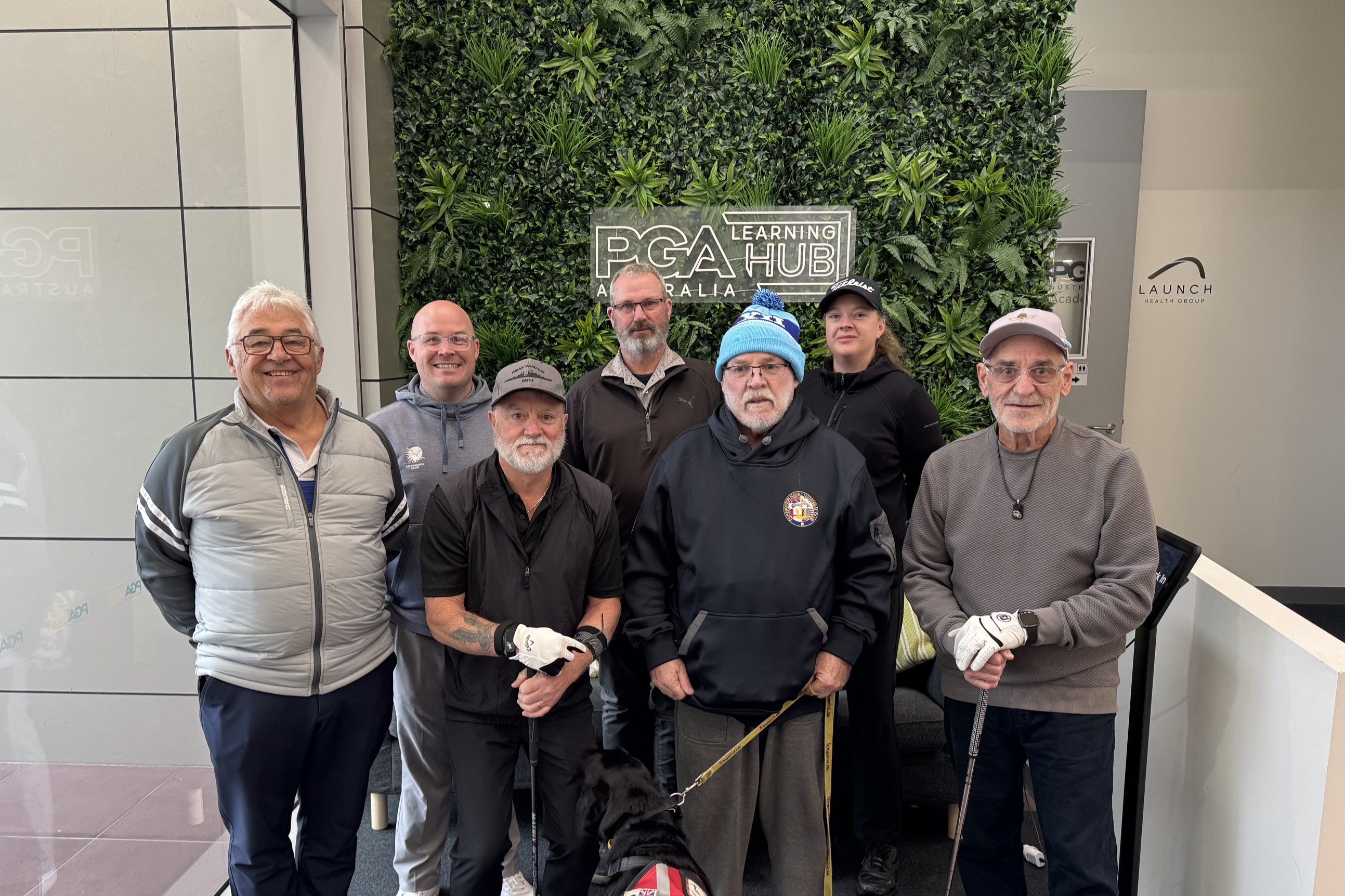 Six veterans standing in front of a wall at PGA of Australia with PGA professional Scott McDermott, taking part in the Fairways to Resilience program