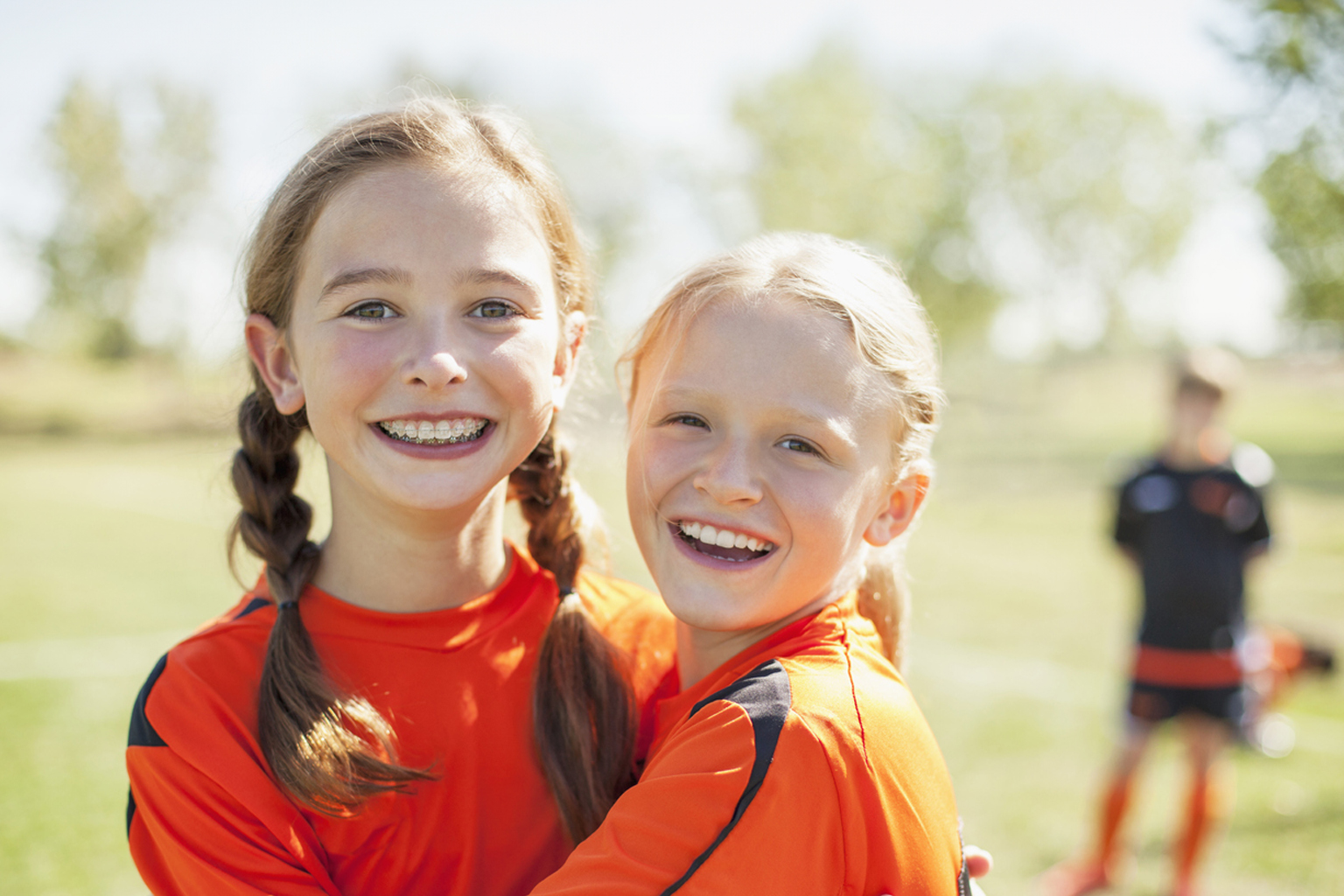 Two young girls embrace while on a sports field